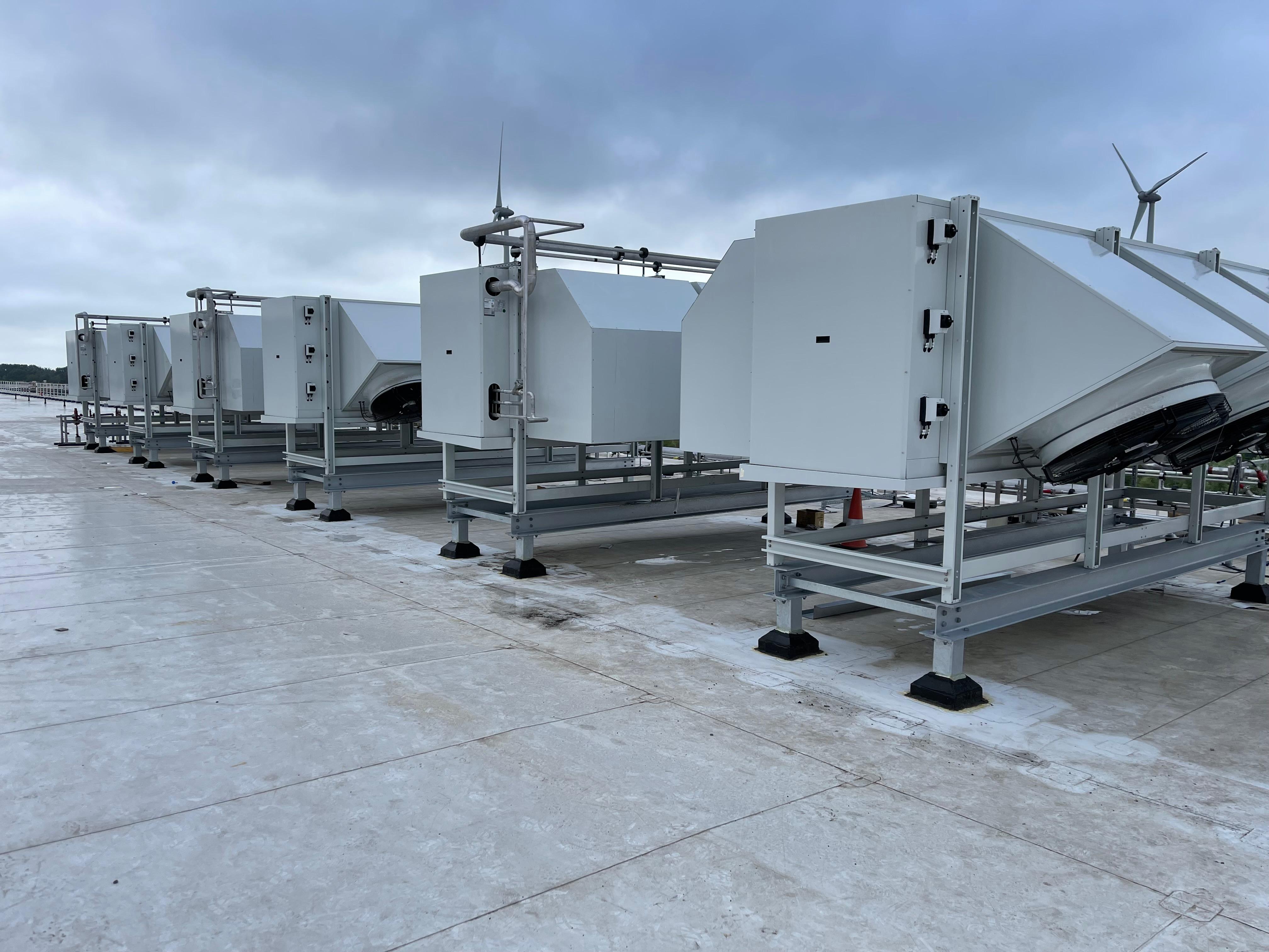 Skids industriais HVAC em cobertura com turbinas eólicas ao fundo