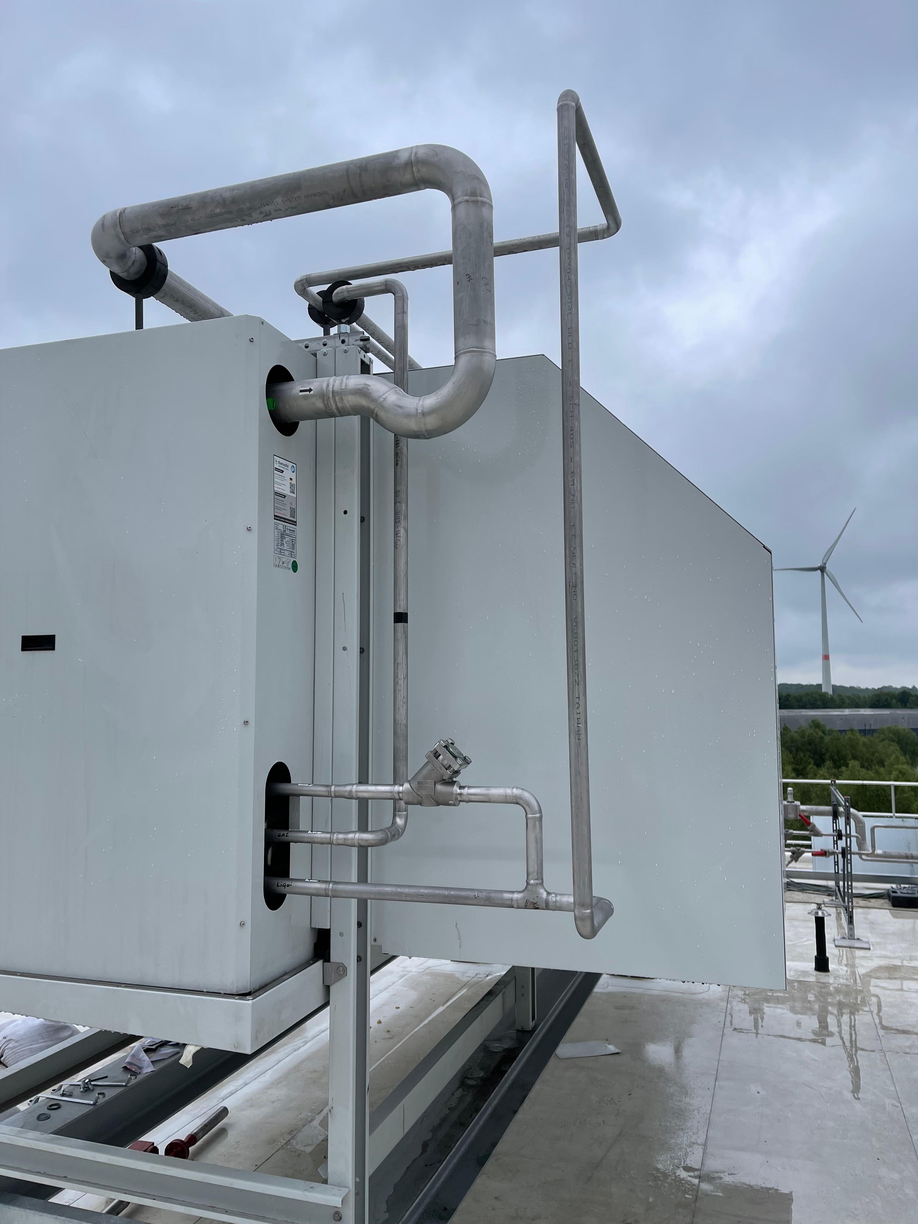 Detalhe de unidade HVAC com tubagem e turbina eólica ao fundo